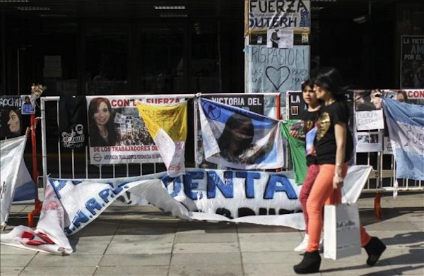Dos jóvenes caminan frente a pancartas de apoyo colocadas por seguidores de la presidenta argentina hoy, miércoles 9 de octubre de 2013, en la entrada de la clínica en donde se encuentra en recuperación la mandataria Cristina Fernández, después de una intervención quirúrgica para drenar un hematoma craneal en buenos Aires (Argentina). Fernández prosigue su recuperación en la unidad de cuidados intensivos de un hospital de la capital tras la operación que se le practicó el martes y que fuentes oficiales calificaron hoy como "perfecta".