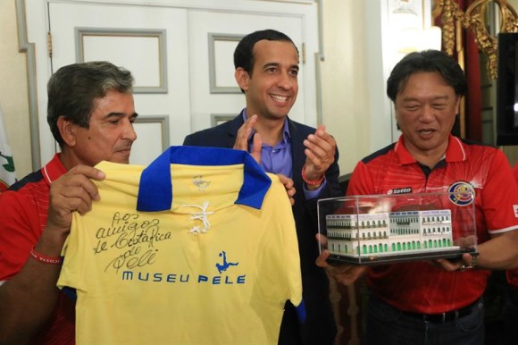 El técnico de Costa Rica, Jorge Luis Pinto (i), muestra una camiseta firmada por Pelé, junto al presidente de la Asociación de Futból de Costa Rica, Eduardo Lee (d), quien sostiene una réplica del museo Rey Pele, en compañía del alcalde de Santos, Paulo Andrade Barbosa (c).
