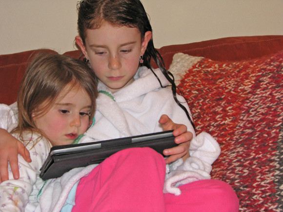 Dos hermanas leyendo un cuentacuentos en su tableta en idioma ingl&eacute;s.
