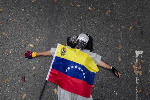 Una mujer permanece en el suelo con una bandera venezolana durante una manifestación convocada por un sector de la oposición venezolana frente a la Nunciatura apostólica por la muerte de un adolescente de 14 años, en Caracas, Venezuela.
