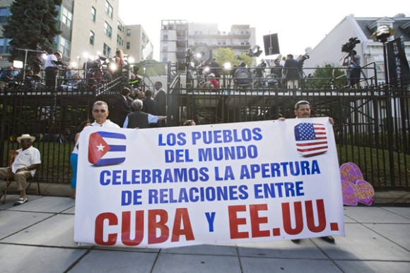 Dos partidarios de la restauraci&oacute;n de las relaciones entre Cuba y Estados Unidos sostienen un cartel frente a la secci&oacute;n de intereses de Cuba donde, por primera vez en 54 a&ntilde;os, la bandera del pa&iacute;s ondear&aacute; en Washington.