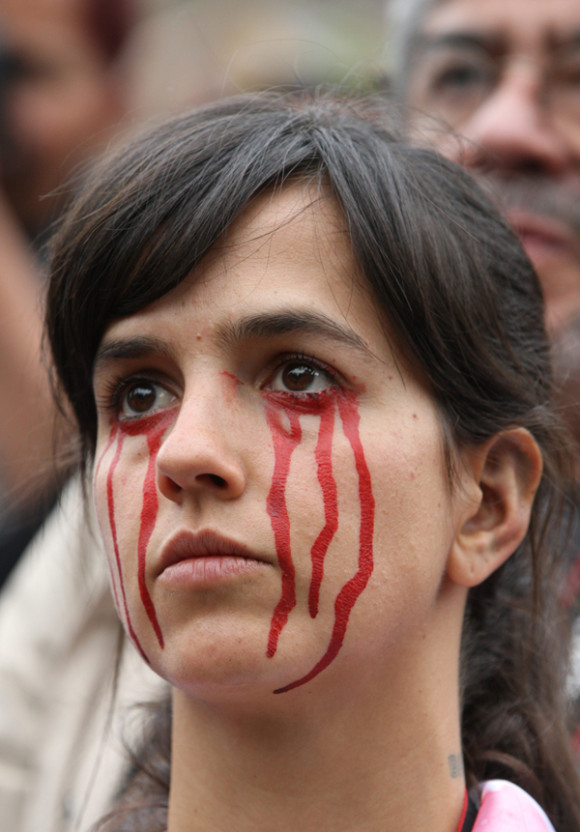 Una joven tiene pintadas lágrimas rojas en su rostro mientras marcha en calles de la Ciudad de México.