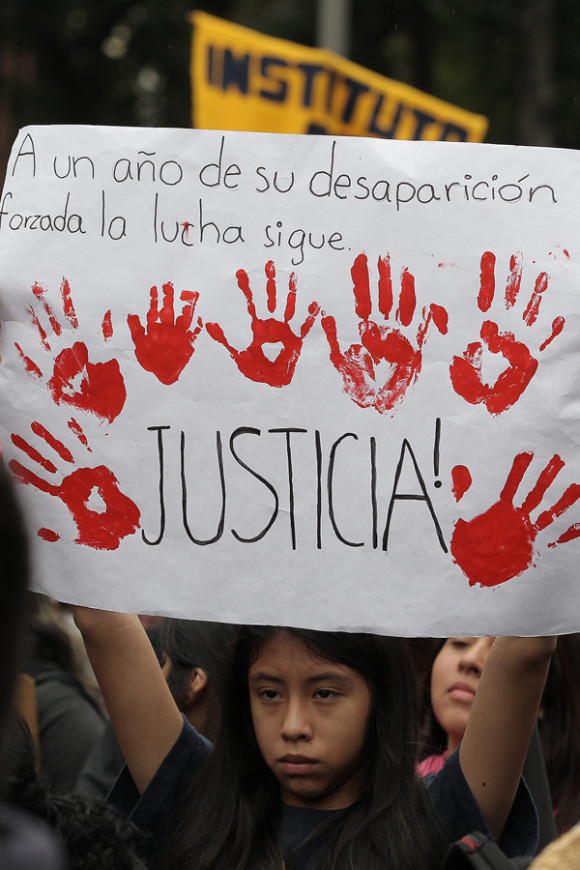 Una joven sostiene una pancarta que dice " A un año de su desaparición forzada la lucha sigue. Justicia" durante una manifestación en calles de la Ciudad de México para recordar el aniversario de la desaparición de 43 estudiantes de la Escuela Normal Rural de Ayotzinapa.