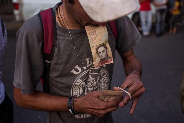 Un hombre organiza sus billetes de 100 bol&iacute;vares mientras hace fila en las inmediaciones del Banco Central de Venezuela.