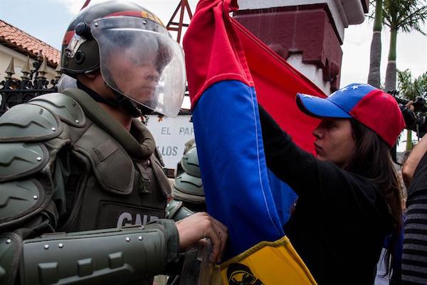 Una mujer sostiene una bandera de Venezuela frente a integrantes de la Guardia Nacional Bolivariana (GNB) durante una manifestaci&oacute;n.