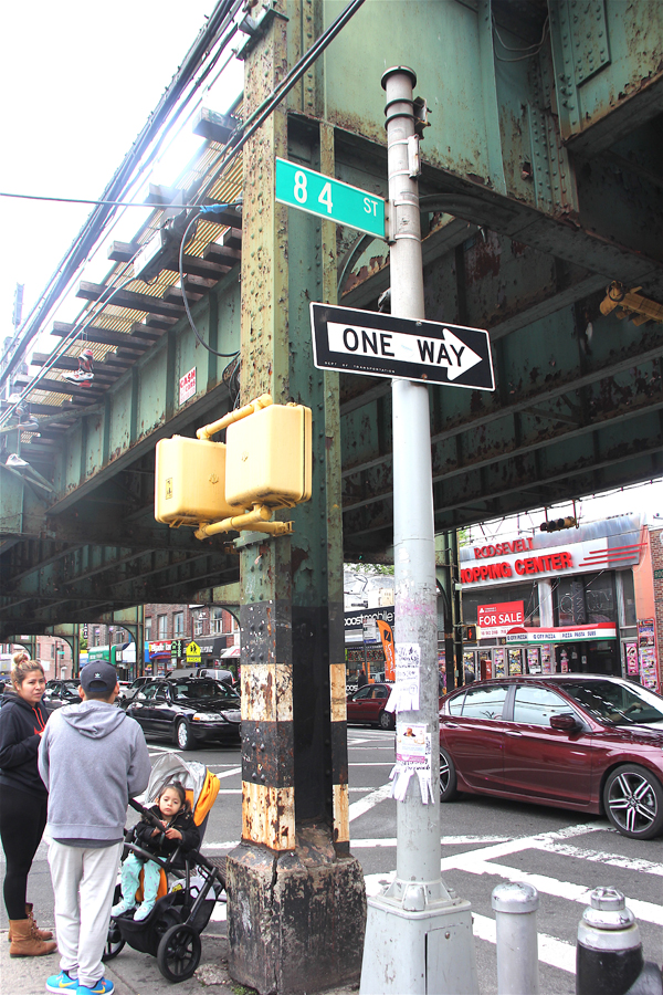 Familias con niños esperan para cruzar la popular Ave. Roosevelt en el condado de Queens, debajo de la estructura del tren 7, algunas llevan alimentos descubiertos y desconocen los efectos del plomo y tóxicos que caen y ponen en riesgo sus vidas.