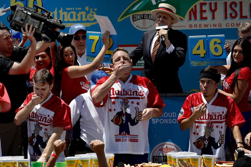 El competidor estadounidense Joey Chestnut (c) come perritos calientes durante el Concurso anual masculino de perritos calientes de Nathan, celebrado en Coney Island, Nueva York
