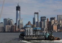 Partes de la punta de la Torre de la Libertad son trasladadas en una barcaza desde Port Newark hacia el bajo Manhattan, donde serán descargadas e instaladas en la parte superior de esta edificación a partir de mañana, en Nueva York.