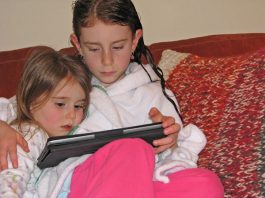 Niños bilingües Dos hermanas leyendo un cuentacuentos en su tableta en idioma inglés.