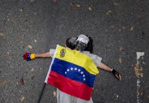 Represión de protestas, detenciones arbitrarias y tortura en Venezuela Una mujer permanece en el suelo con una bandera venezolana durante una manifestación convocada por un sector de la oposición venezolana frente a la Nunciatura apostólica por la muerte de un adolescente de 14 años, en Caracas, Venezuela.