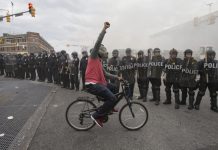 Un hombre monta bicicleta frente a una barrera de policías durante una protestas por la muerte de Freddie Gray en Baltimore.