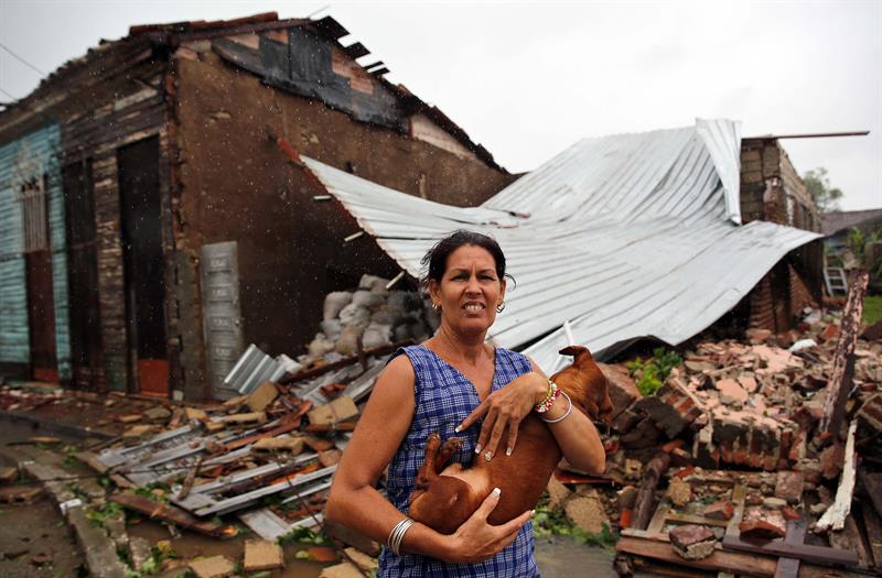 Una mujer posa con su perro frente a su casa destruida por el paso del hurac&aacute;n Irma,