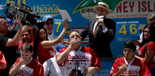 El competidor estadounidense Joey Chestnut (c) come perritos calientes durante el Concurso anual masculino de perritos calientes de Nathan, celebrado en Coney Island, Nueva York