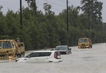 Camiones de la Guardia Nacional de Texas que llevan a víctimas de inundaciones pasan junto a vehículos sumergidos después del paso del huracán Harvey en Houston, Texas