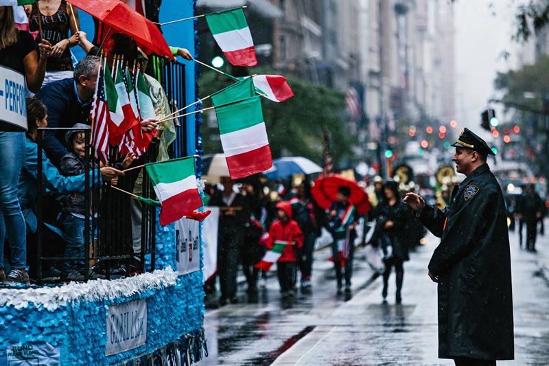 Un oficial de polic&iacute;a (d) saluda a los asistentes que sostienen banderas italianas durante una marcha por al Quinta Avenida, durante el Desfile Anual del Columbus Day, en Nueva York 