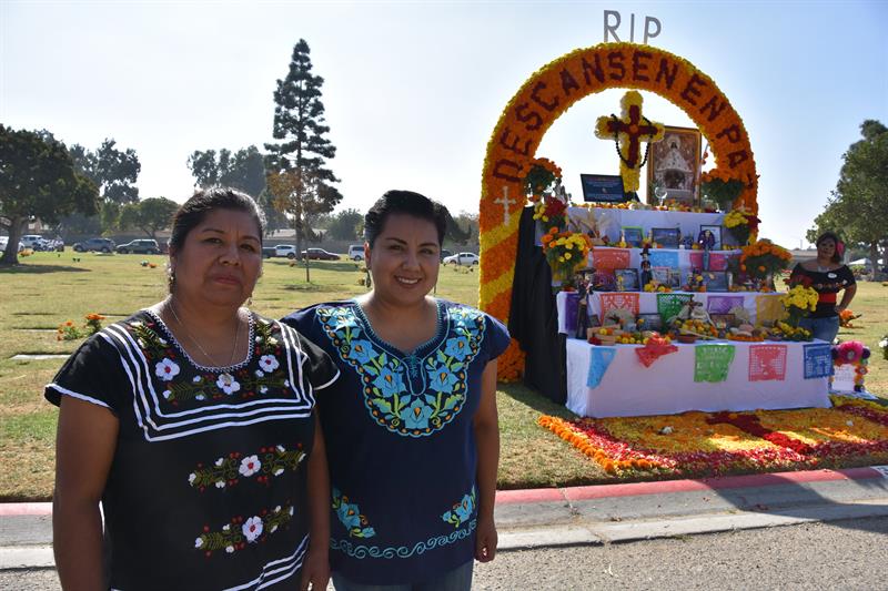 Flora de los Santos, originaria de Oaxaca, posa junto a su hija, frente al altar que han decorado, en el cementerio Santa Clara de Oxnard.