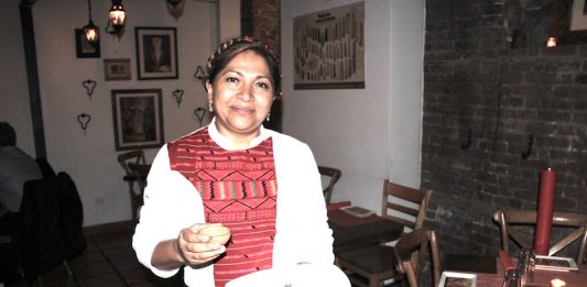 La Chef Olga Cabrera muy emocionada de presentar por primera vez en Café Frida de Nueva York, la auténtica cocina mixteca, sostiene un Nicuatole con nopalitos en almíbar y una pequeña jícara con whisky de maíz Pierde Almas Ancestral.