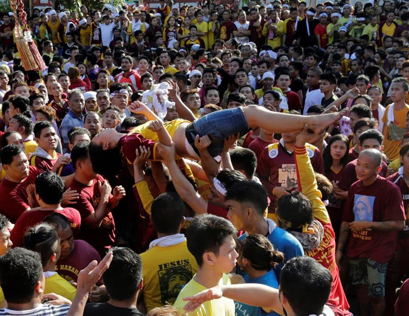 Una mujer que cayó inconsciente entre la multitud es llevada por un grupo de personas en medio de miles devotos católicos durante la procesión de El Nazareno Negro.