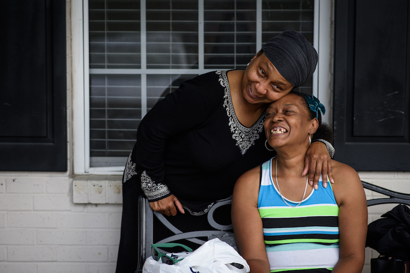 Jean Moore (izquierda) comparte una risa con su hermana, Ruby Wilson, frente al centro de vida asistida donde vive Wilson. (Andrew Craft para Kaiser Health News)