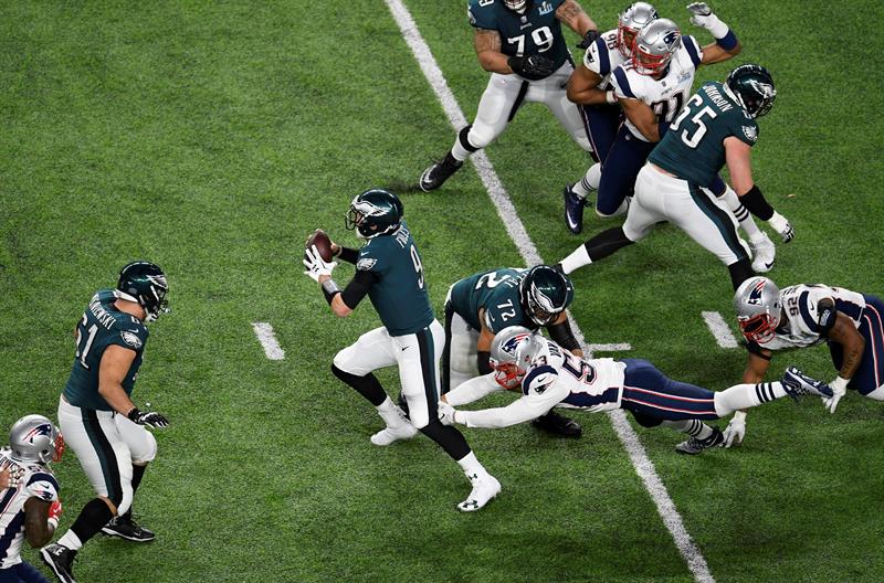 El mariscal de campo de los Philadelphia Eagles Nick Foles (C) se revuelve mientras el linebacker exterior de los New England Patriots Kyle Van Noy (R) persigue durante el Super Bowl LII en el US Bank Stadium en Minneapolis, Minnesota