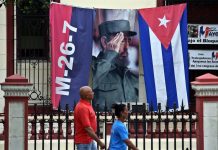 Cuba, entre la expectación y la rutina ante un histórico relevo presidencial Dos personas caminan junto a un lienzo con la imagen del fallecido líder cubano Fidel Castro en una calle de La Habana