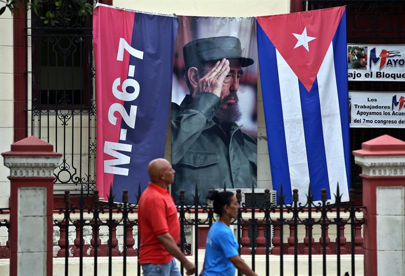 Dos personas caminan junto a un lienzo con la imagen del fallecido l&iacute;der cubano Fidel Castro en una calle de La Habana