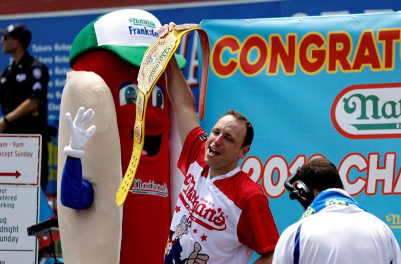 El estadounidense Joey Chestnut (c) participa en un concurso de comer perritos calientes en Nueva York