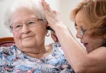 Janie York examina el oído de Elaine Martin en SilverRidge Assisted Living, en Gretna, Nebraska, en agosto. Martin tenía bastante cera en sus oídos, antes que York le realizara una limpieza y comenzara a usar audífonos. Ahora, York le limpia los oídos a Martin con regularidad. (Chris Machian para KHN)