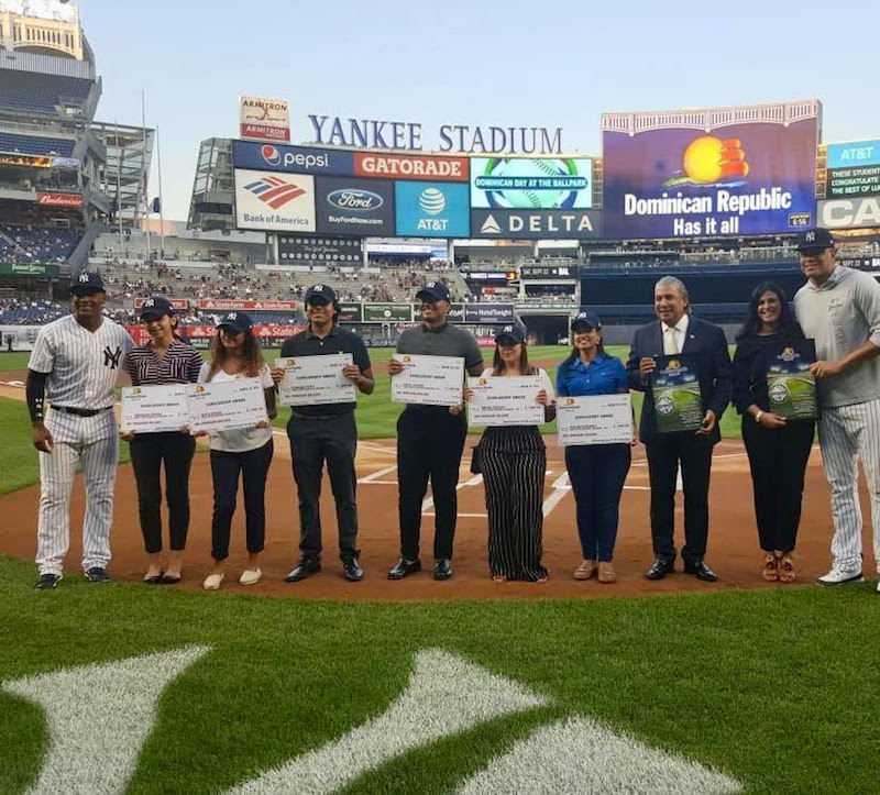 El c&oacute;nsul Carlos Castillo, tercero desde derecha, junto a Lucien Echavarr&iacute;a en el terreno de juegos con los estudiantes becados y los peloteros Miguel And&uacute;jar y Dellin Betances.