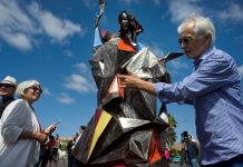 Jim Bliesner (d) posa junto a una réplica en miniatura de su obra "Bienvenido al Extraño", que retrata a la virgen María sujetando una antorcha y ataviada con una túnica de acero