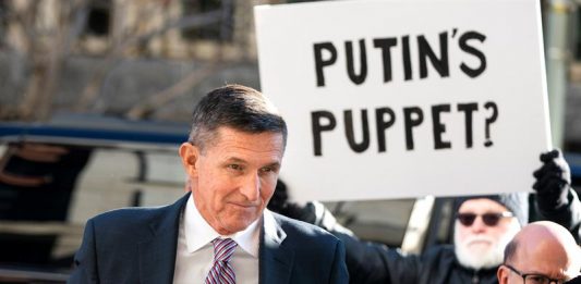 El ex asesor de Seguridad Nacional estadounidense Michael Flynn, a su llegada al Tribunal Federal, mientras un manifestante (c) sostiene una pancarta en la que puede leerse ''¿La marioneta de Putin?''