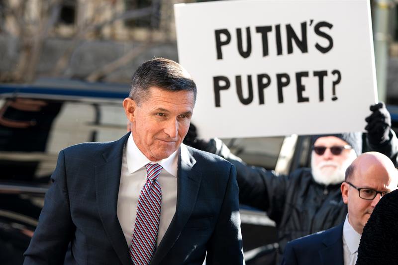  El ex asesor de Seguridad Nacional estadounidense Michael Flynn, a su llegada al Tribunal Federal, mientras un manifestante (c) sostiene una pancarta en la que puede leerse ''&iquest;La marioneta de Putin?''