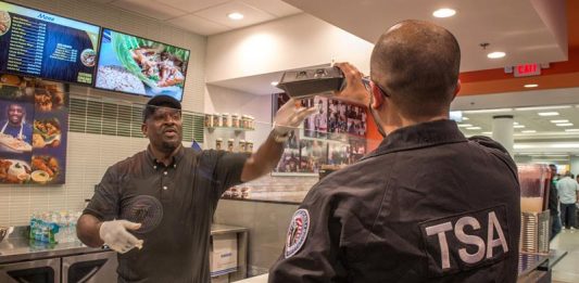 Un agente de la Administración de Seguridad del Transporte (TSA) recibe comida gratuita de manos de Wilkinson Sejour, dueño de Chef Créole.