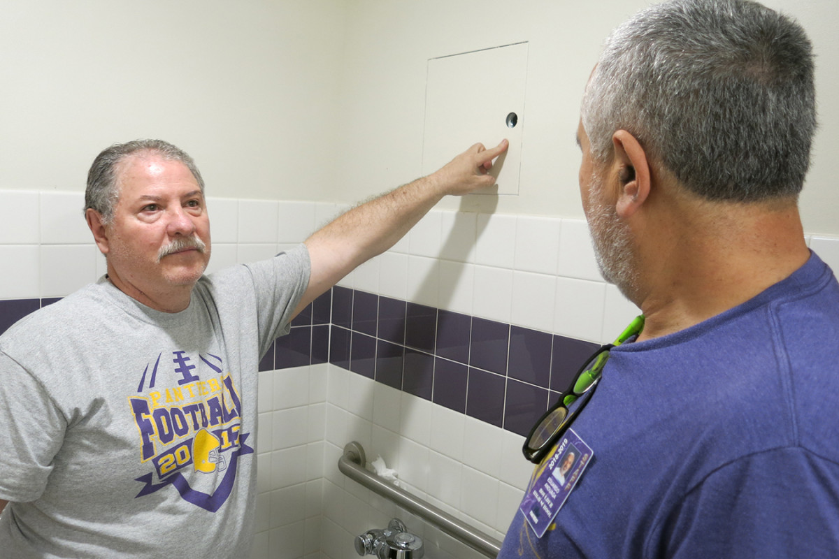 El custodio de Boulder High, Allen Chávez, muestra un agujero en la pared del baño de varones en donde los estudiantes dejan productos de vapeo. Dijo que los encuentra por toda la escuela. (John Daley/Colorado Public Radio)