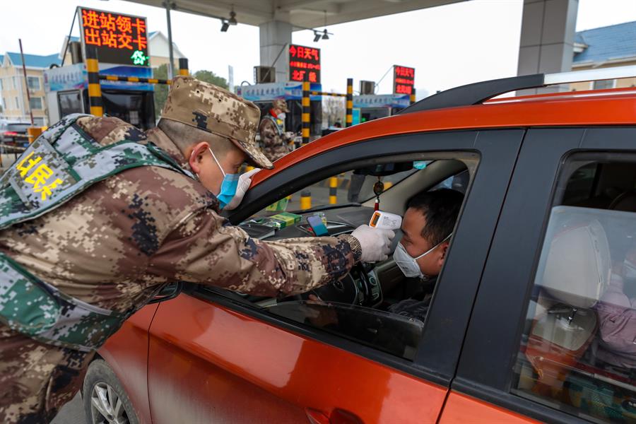 Un miembro de la milicia verifica la temperatura corporal de un conductor en un veh&iacute;culo en una autopista de peaje en Wuhan, provincia de Hubei, en el centro de China, el 23 de enero de 2020.