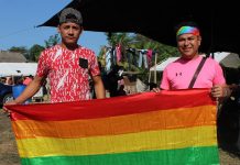 Los activista LGBT José Vázquez (i) y Mavisa (d), quienes viajan en la caravana de migrantes hondureños, posan con la bandera de arcoíris.