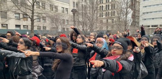 Vestidas de negro, con los ojos vendados y complementos de color rojo, las mujeres, de colectivos feministas y latinos, escenificaron la coreografía y gritaron en inglés y español "el violador eras tú".