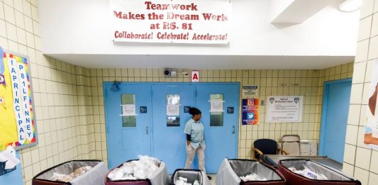 Una mujer espera en la puerta del colegio 234 de Queens para recoger la comida que desde este viernes ofrece el Ayuntamiento de Nueva York a toda persona que lo necesite