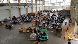 Sentados en varias hileras de mesas entre el eco de las voces, el ruido de la manufacturaci&oacute;n en cadena y de la m&uacute;sica proveniente de los altavoces de algunos de los voluntarios, 160 personas fabrican entre 25.000 y 30.000 m&aacute;scaras protectoras al d&iacute;a.