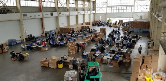 Sentados en varias hileras de mesas entre el eco de las voces, el ruido de la manufacturación en cadena y de la música proveniente de los altavoces de algunos de los voluntarios, 160 personas fabrican entre 25.000 y 30.000 máscaras protectoras al día.