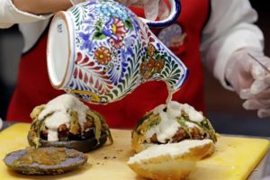 Una mujer prepara una hamburguesa que lleva los ingredientes del tradicional chile en nogada