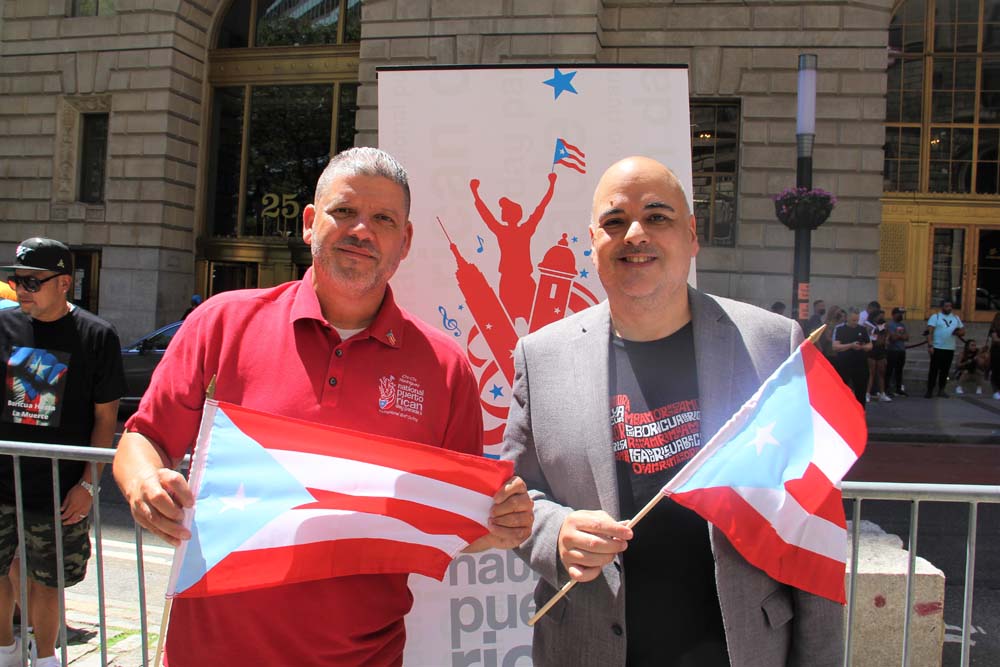 Louis Miranda, quien preside el directorio del Desfile Nacional Puertorriqueño de Nueva York, junto a otro directivo de la organización, posaron felices con su amada bandera, durante la izada de su pabellón en Bowling Green.