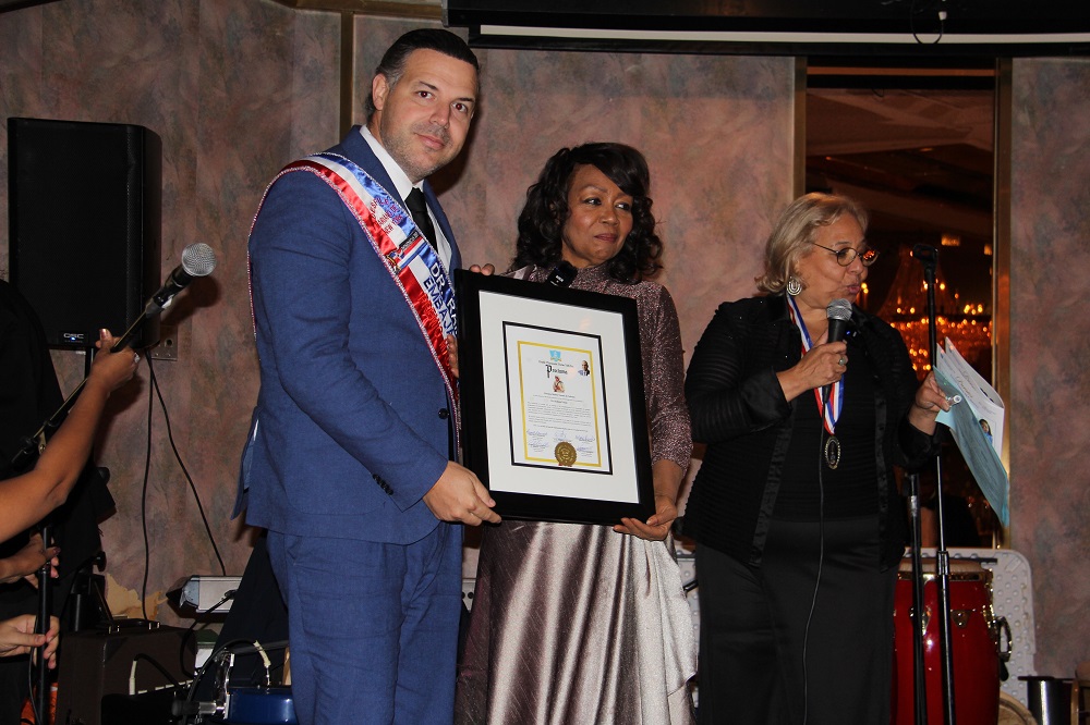 El Dr. Ram&oacute;n Tallaj estuvo representado por su hijo, Dr. Ram&oacute;n Tallaj Jr., quien recibi&oacute; el reconocimiento de los organizadores del Desfile Mariano en nombre de su famoso padre. Junto a &eacute;l, la fundadora de la agrupaci&oacute;n, Altagracia Giraldo y Dona Mary Khury.