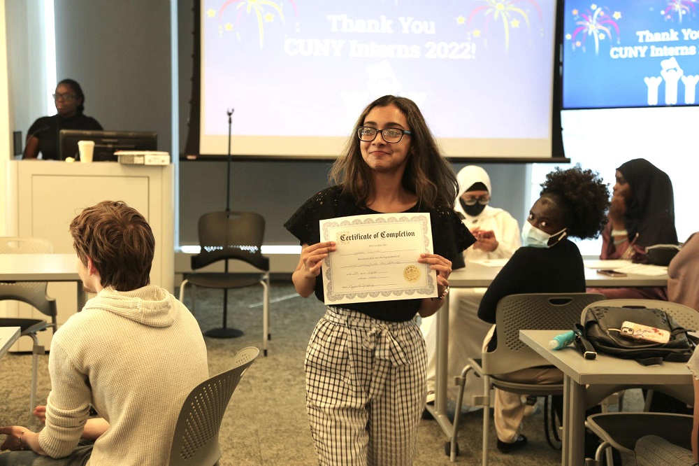 Una joven pasante de CUNY posa con su Certificado de finalización de PEU del verano 2022 durante la ceremonia de clausura.