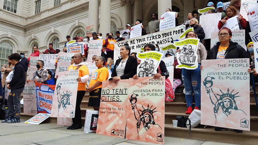 Decenas de inmigrantes y activistas sostienen pancartas que piden vivienda en vez de carpas para los inmigrantes