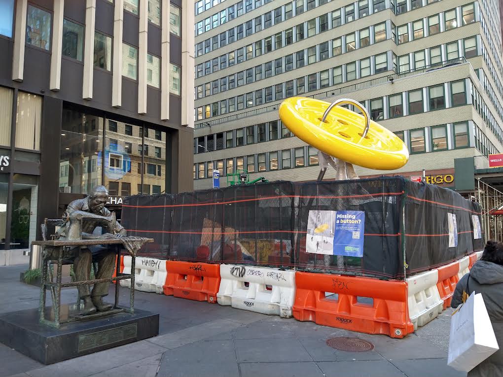 BOTON GARMENT DISTRICT (portada) Muchos habitantes de la ciudad de Nueva York, extrañaban el gigantesco botón atravesado por una colosal aguja que acompañaba a la escultura del costurero judio en la Séptima Avenida con la calle 39 en Manhattan, corazón del Distrito de la Costura o Distrito de la Moda.