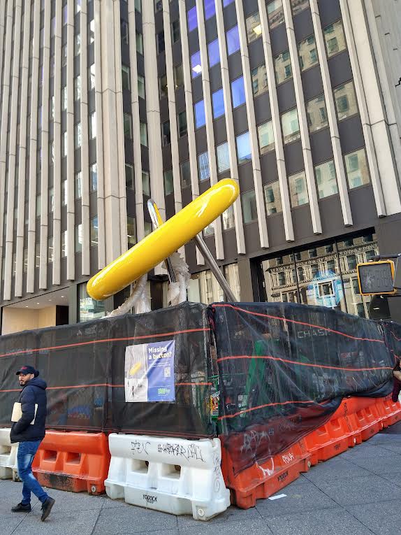 A través de las mallas que protegen la instalación del nuevo monumento del Botón y la Aguja en el Distrito de la Confección en Manhattan, es posible apreciar el colorido de la misma, que evoca a los clásicos taxis neoyorquinos.