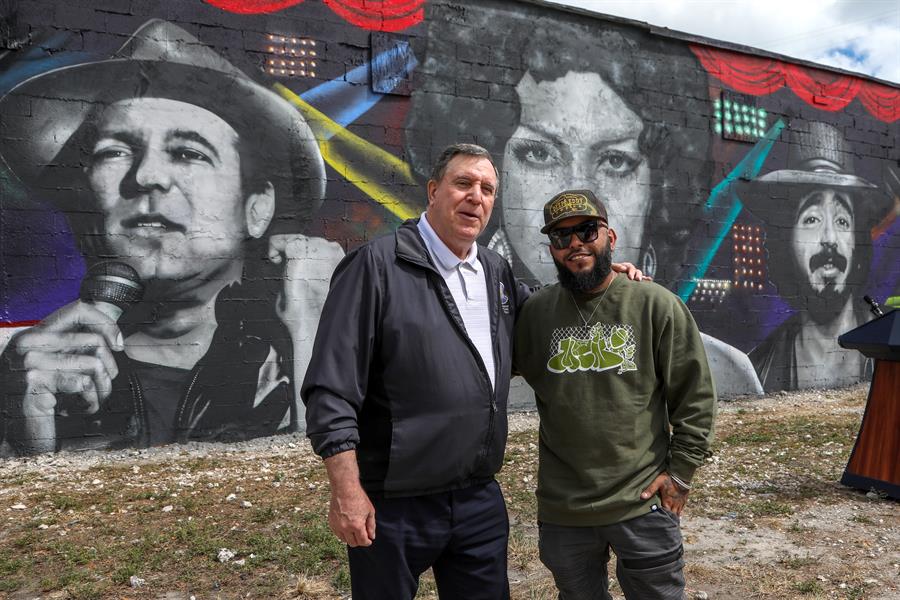 El artista venezolano Pedro Aguiar (d), conocido en el ambiente artístico como CYST1, posa frente a su mural acompañado por el comisionado de Miami