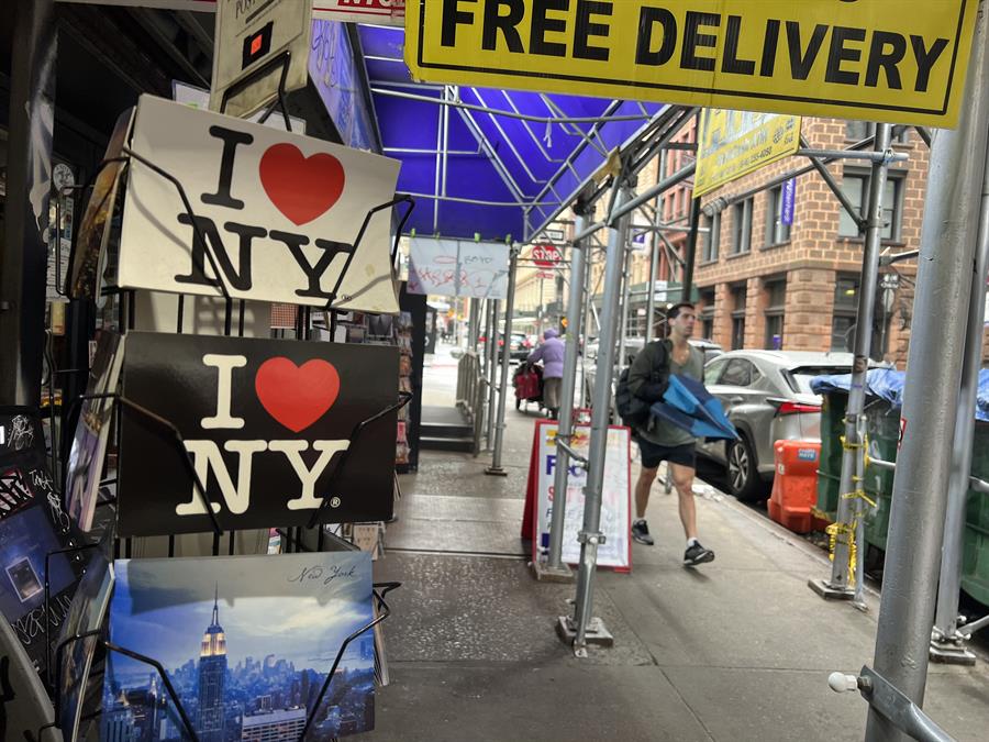 Personas caminan frente a tiendas que venden postales con el tradicional logo I Love NY