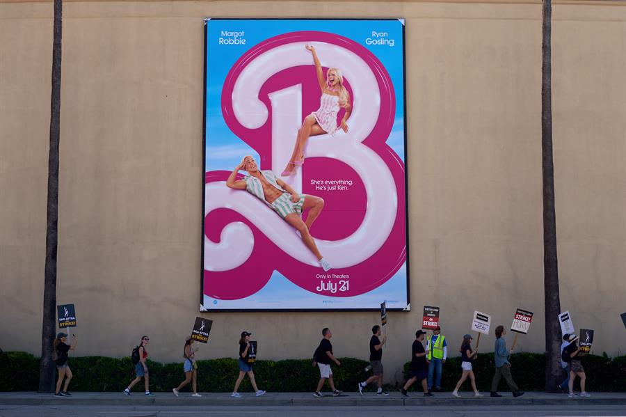 Artistas de Televisión y Radio que se manifiestan con miembros del WGA (Writers Guild of America) pasan junto a un póster de la película Barbie